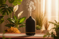Black essential oil diffuser emitting mist on a blurred background