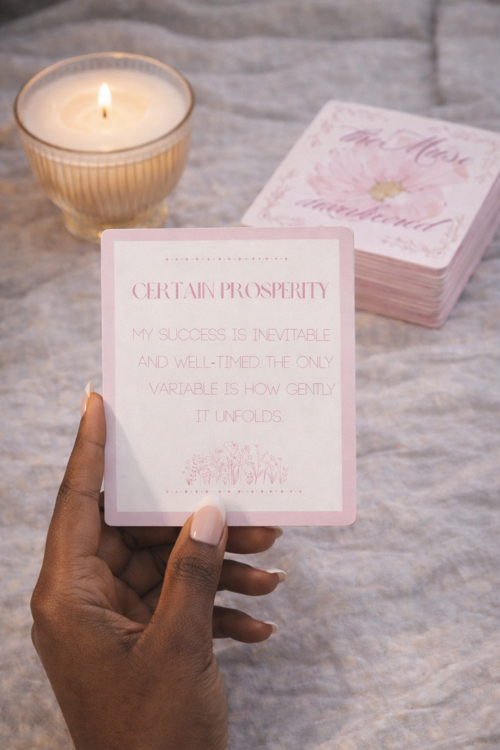 Hand holding a pink card with text, candle in the background